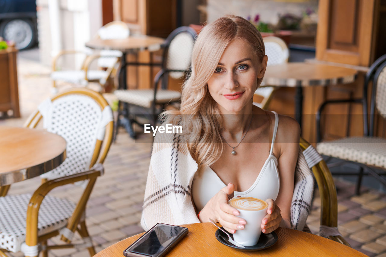 Young beautiful woman, in cafe, drinking coffee in cup, in cozy plaid happy