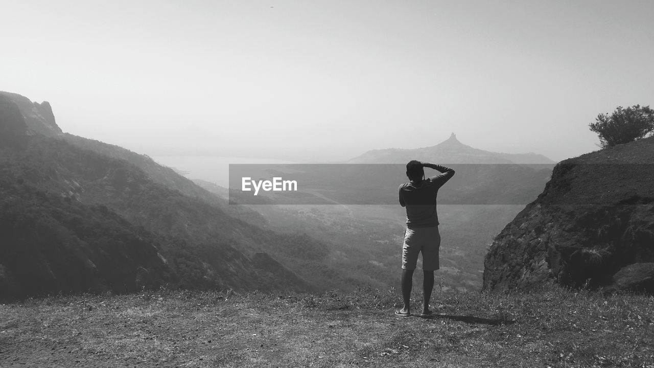 Rear view of man standing on mountain against sky