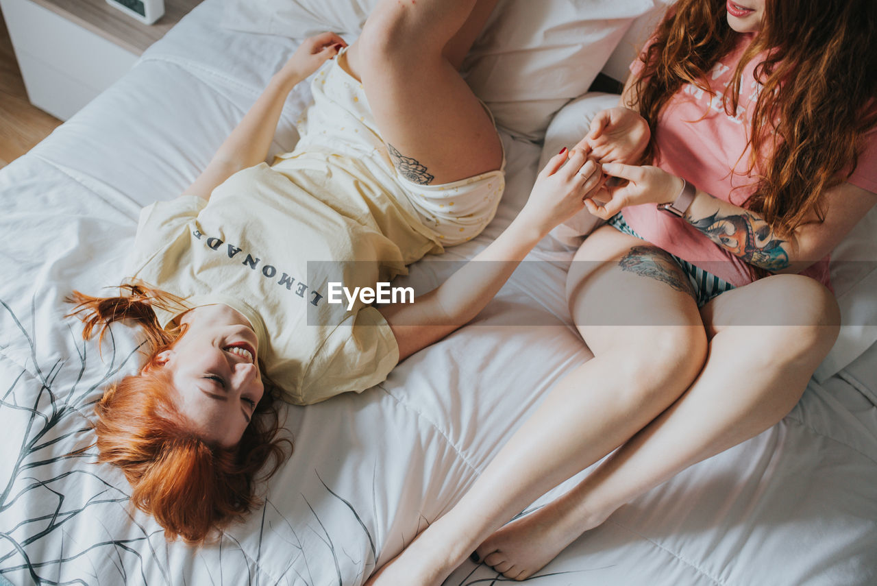 Crop young female girlfriends in pajamas relaxing on bed in bedroom