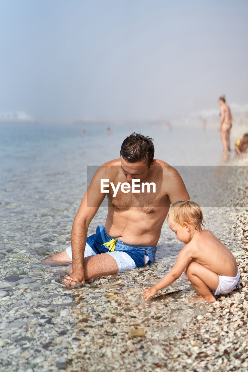 rear view of shirtless man sitting on beach