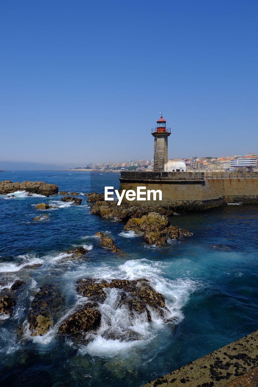 Lighthouse by sea against clear sky