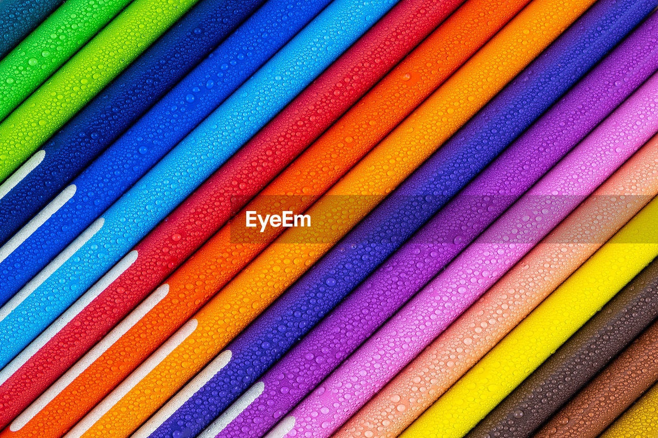 Multicolored pencils with water drops on wooden table, top view, selective focus