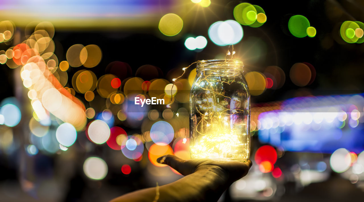 Cropped hand of person holding illuminated lights in jar