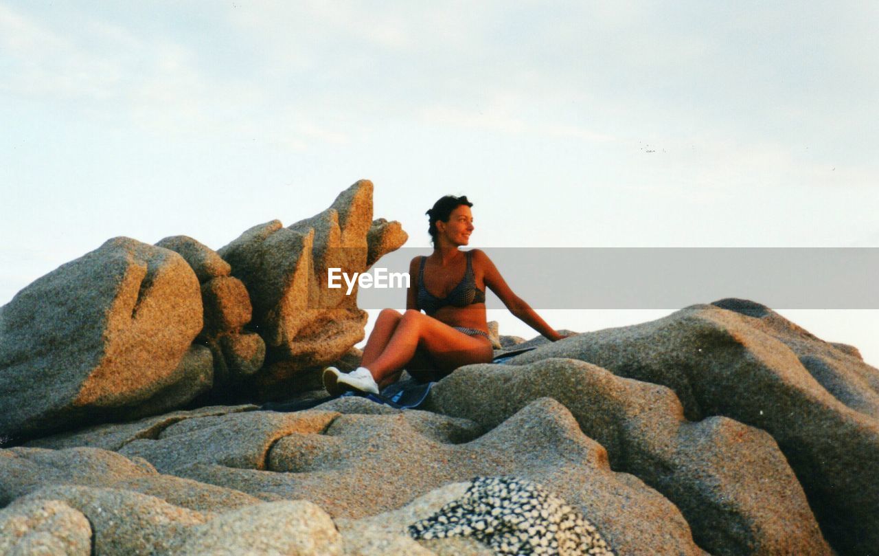 FULL LENGTH OF YOUNG WOMAN SITTING ON ROCK