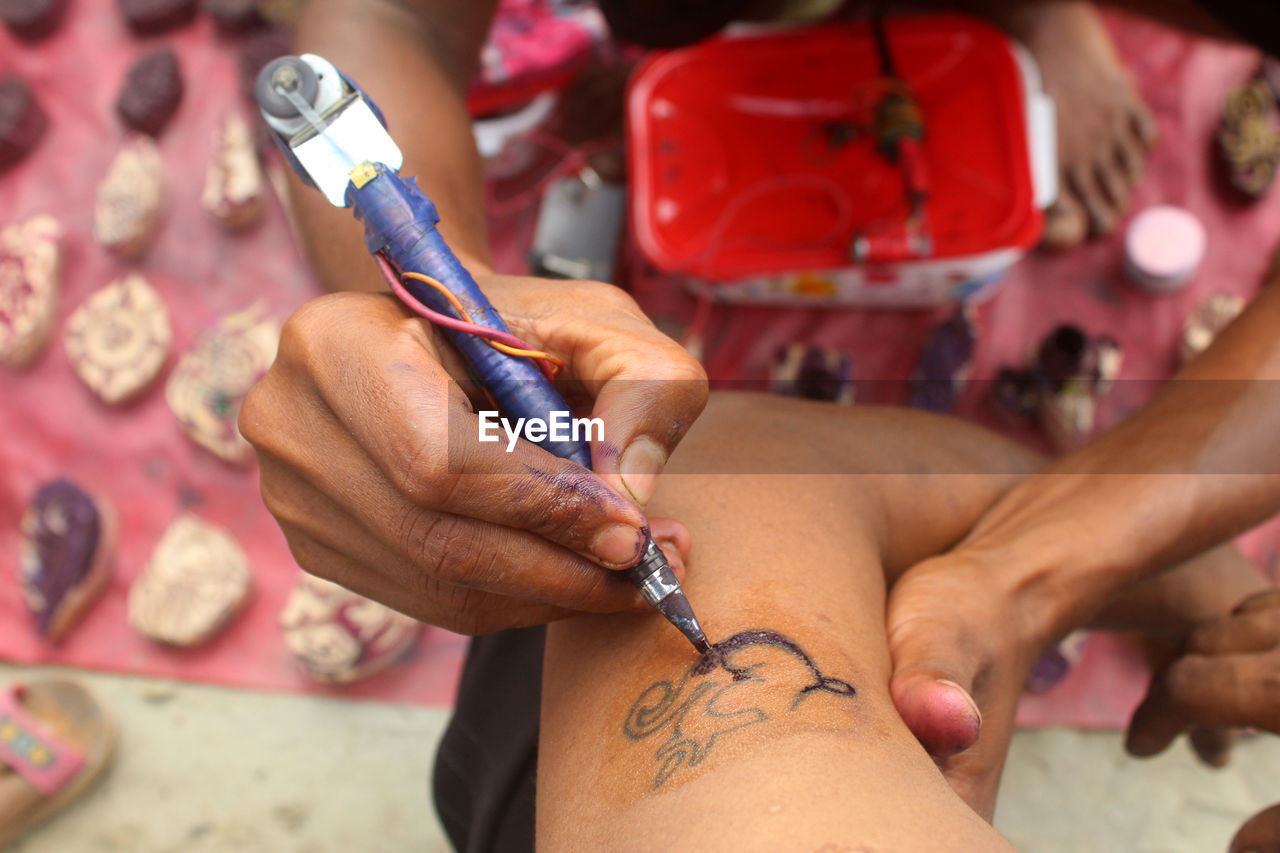 High angle view of hands making tattoo on customer