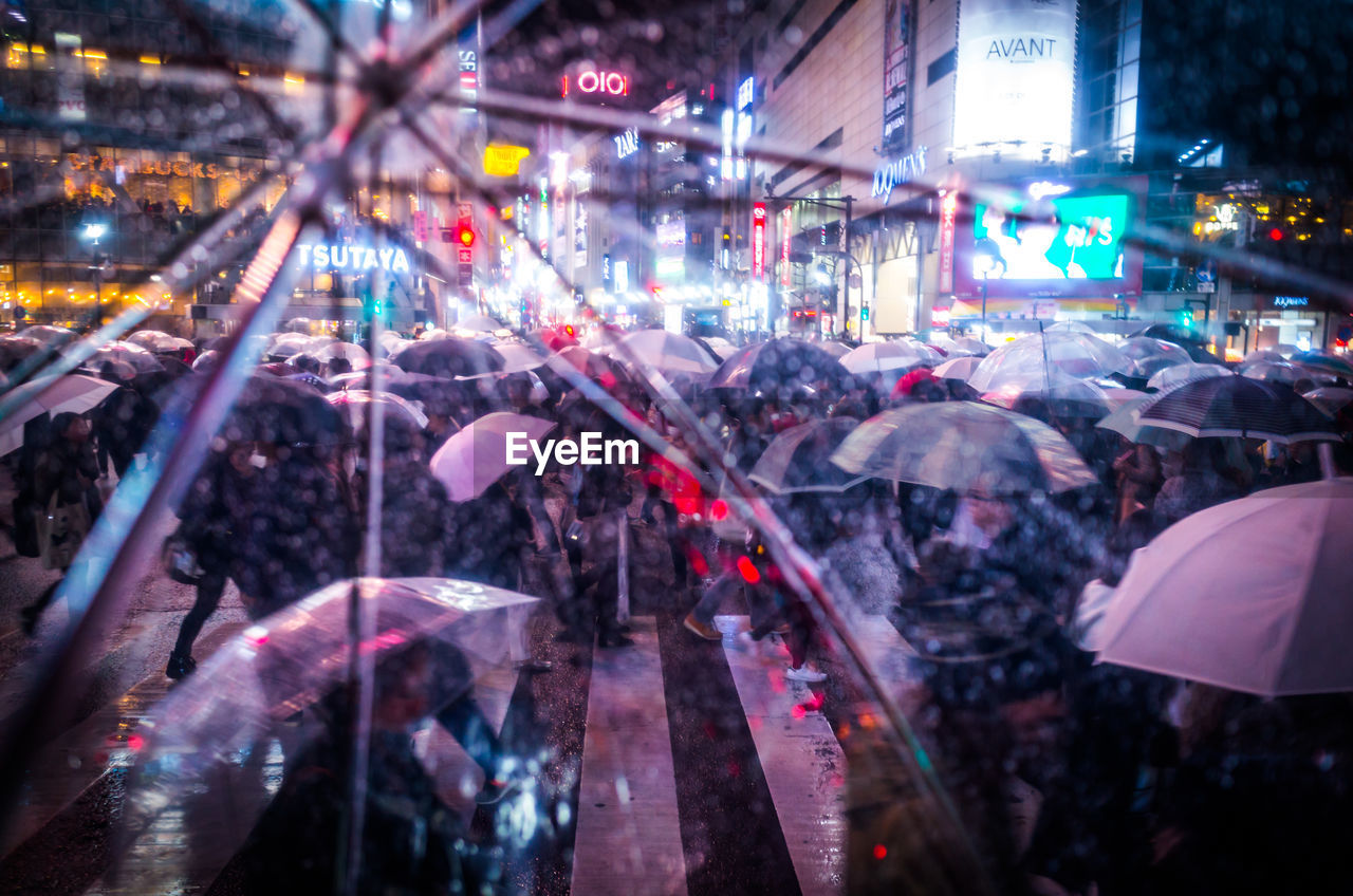 People on city street at night seen though umbrella during rainy season