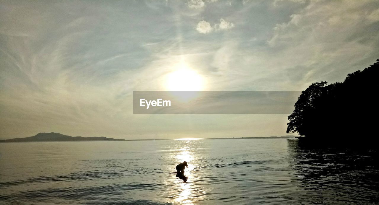 Silhouette woman in sea against sky during sunset