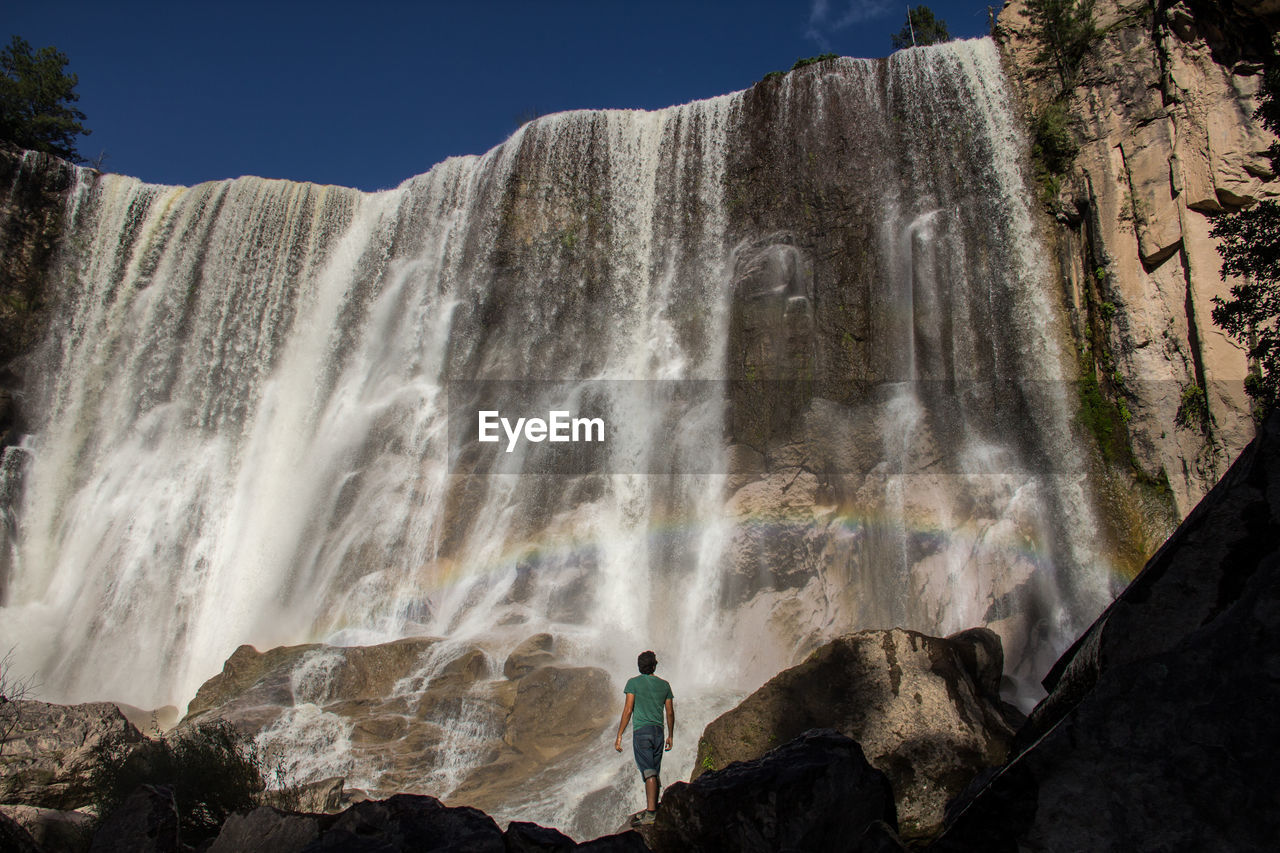 Rear view of man standing against waterfall