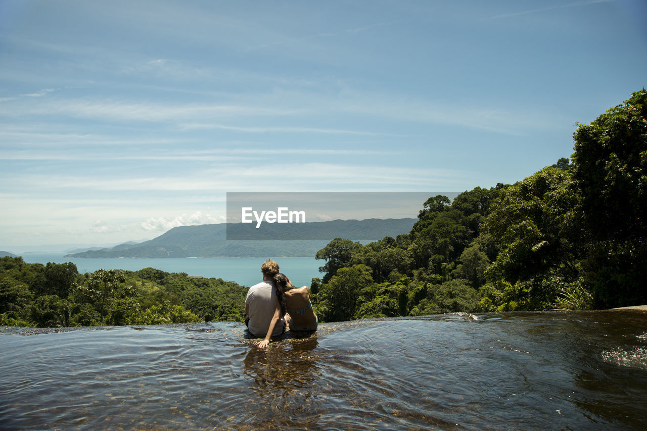 Couple sitting by the waterfall and looking at sea