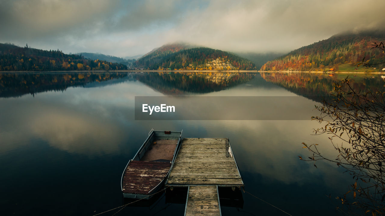 Boat moored by jetty on lake against cloudy sky