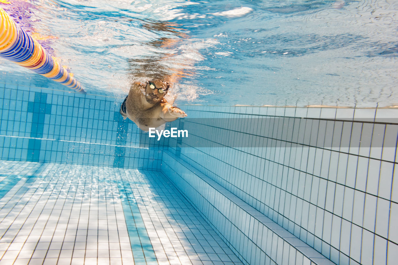 Shirtless man swimming underwater in pool