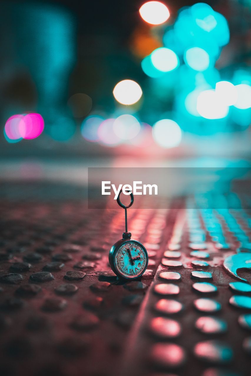 Close-up of pocket watch on footpath in illuminated city at night