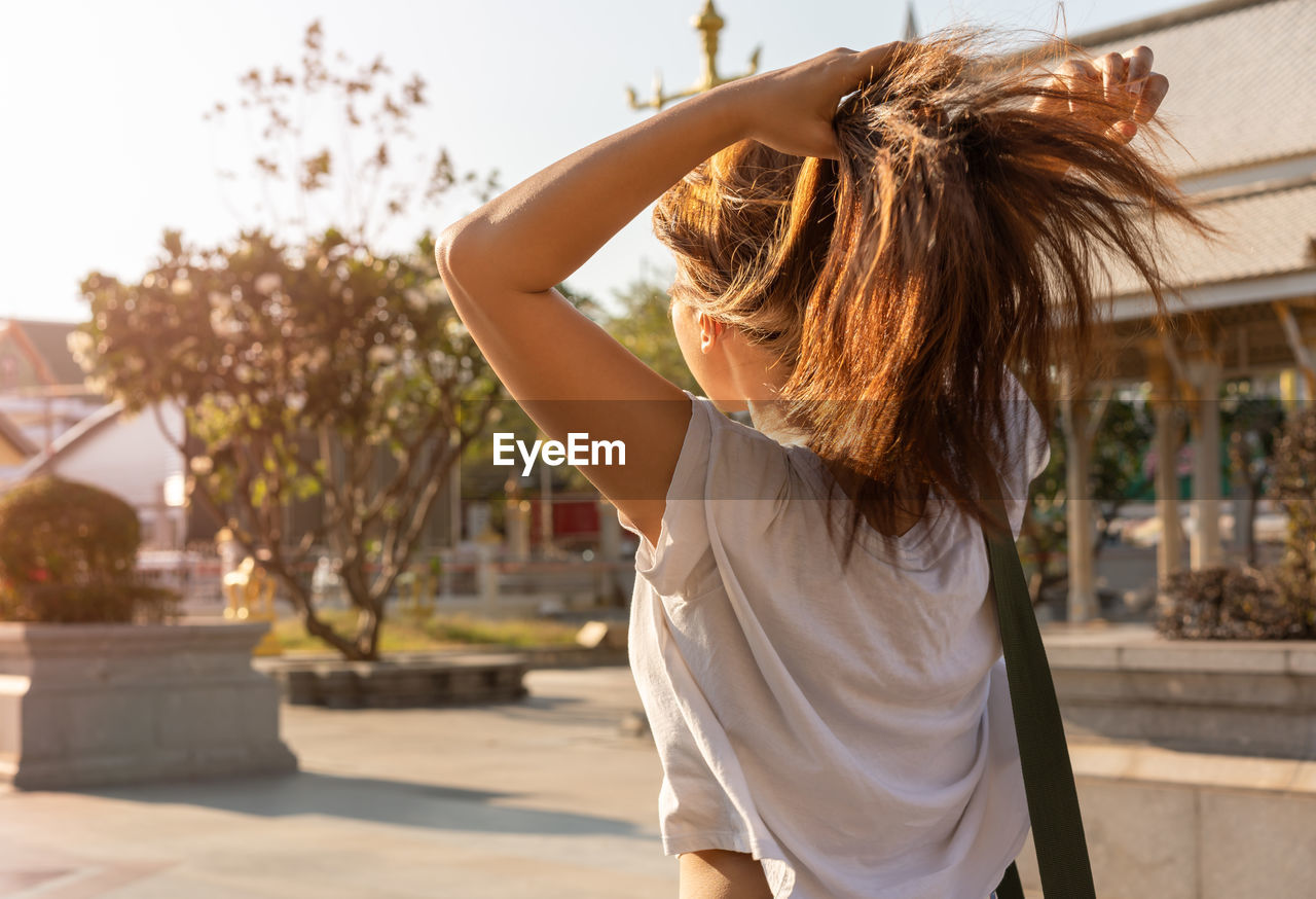 Rear view of woman tying hair while standing in park