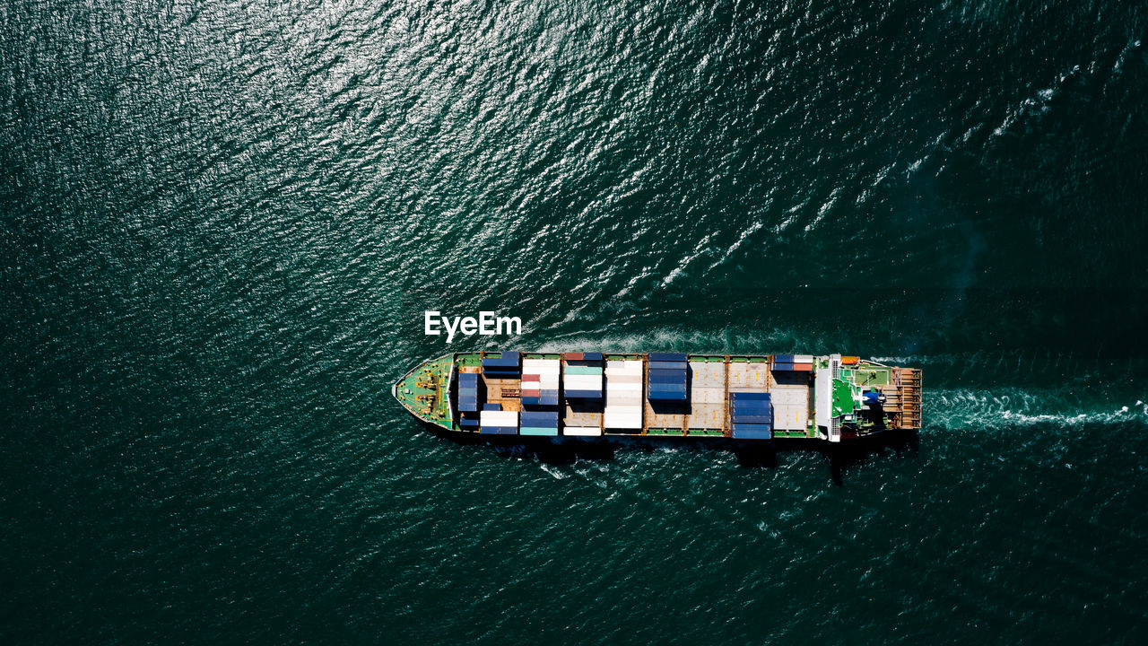 Aerial top view container ship sailing on the green sea full speed container for logistics, 