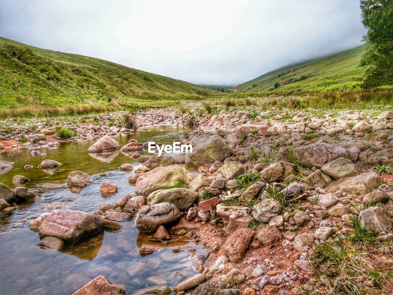 Scenic view of stream flowing by mountain against sky