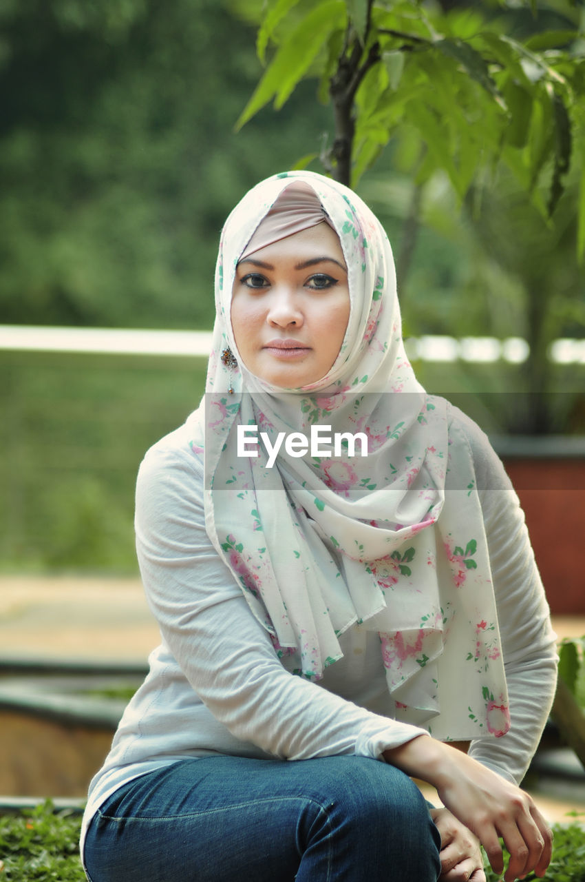 Portrait of young woman in hijab sitting at park