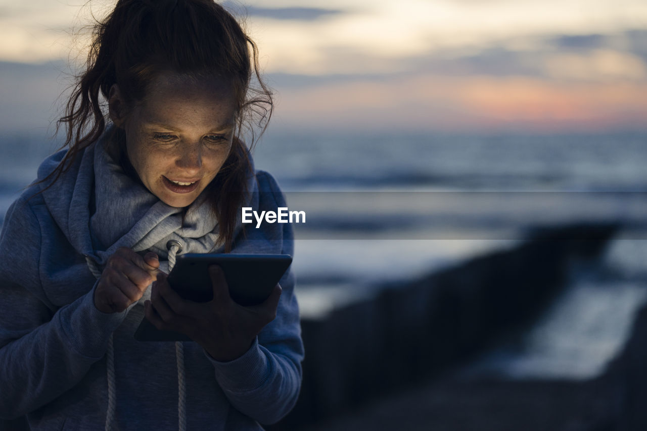 Woman using digital tablet on the beach at sunset