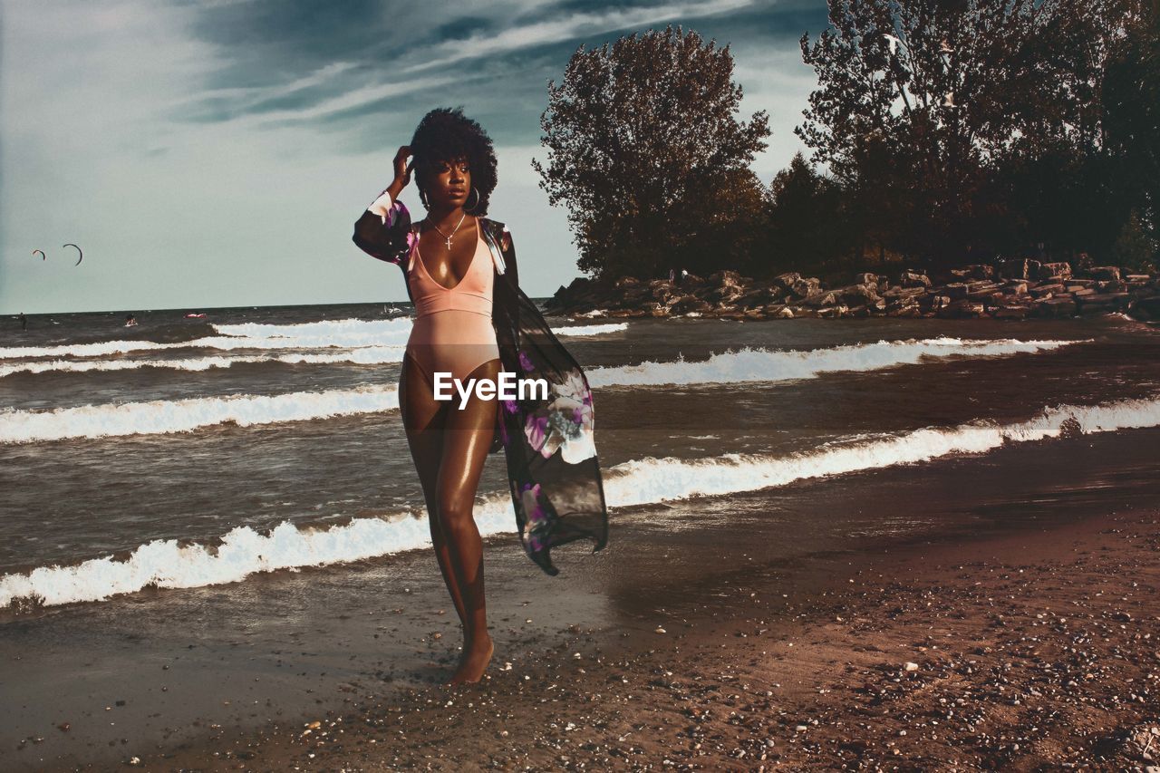 Young woman standing at beach against cloudy sky