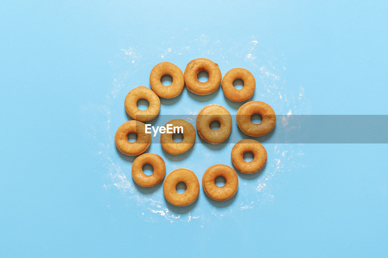 Yeast raised doughnuts aligned in circle shape, on blue background. ring donuts on kitchen table. 