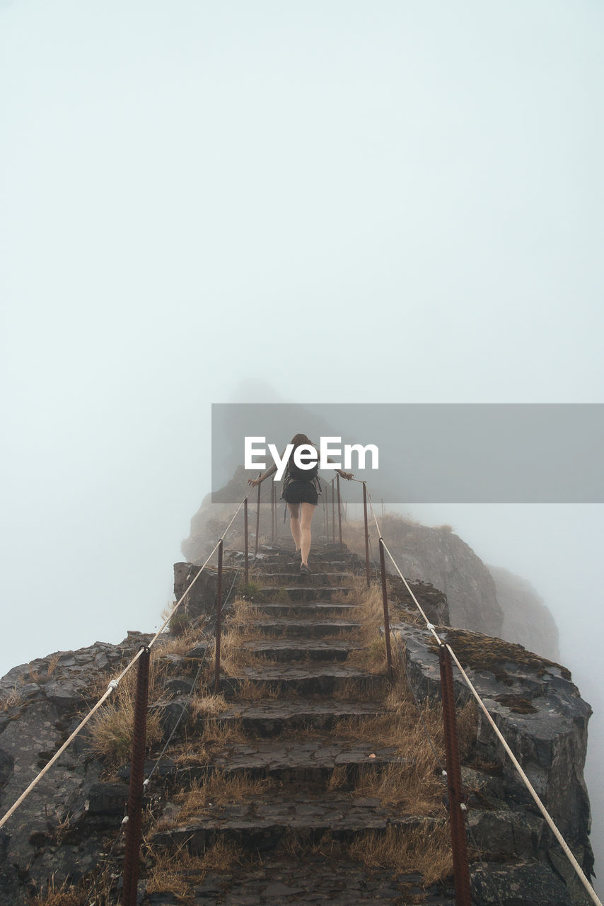 Low angle view of woman on steps against sky during foggy weather