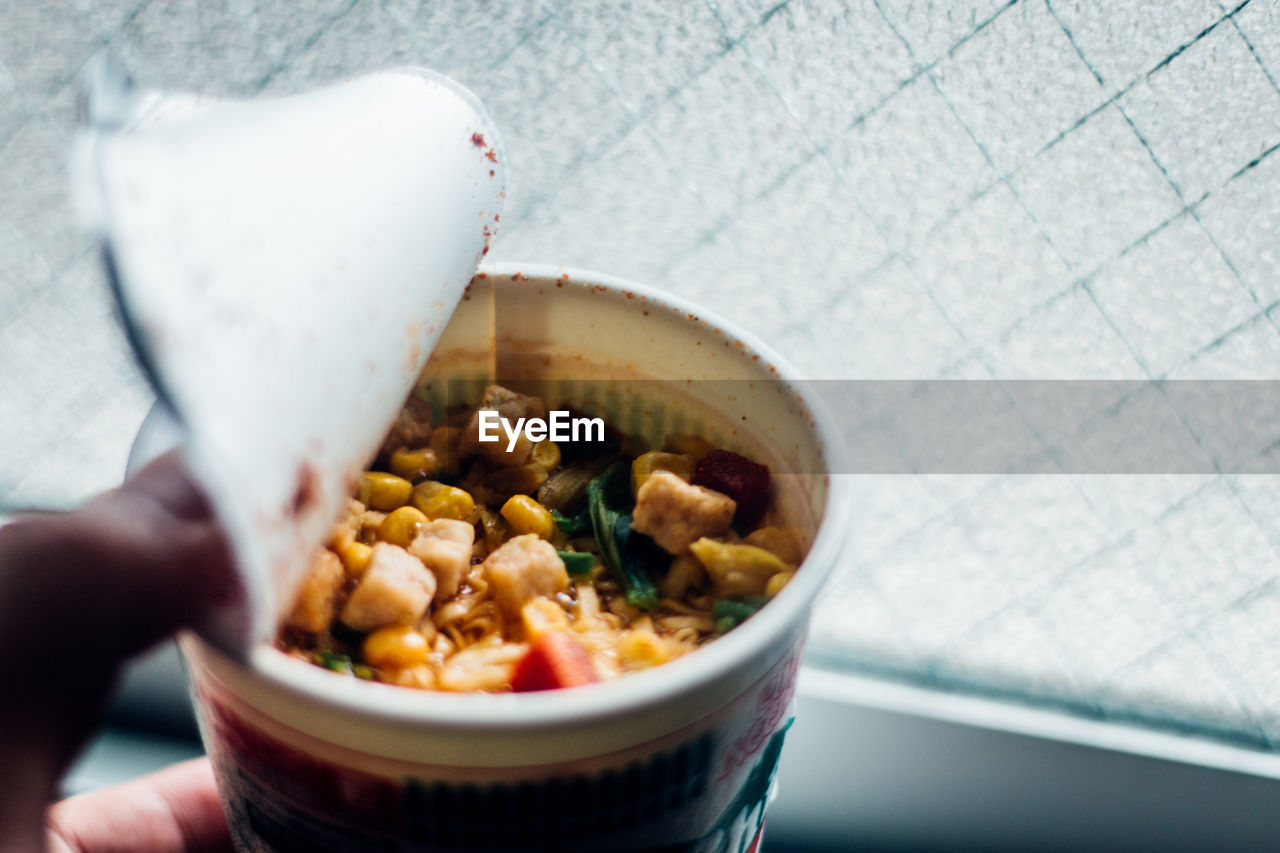 Cropped fingers of person holding food in container by window