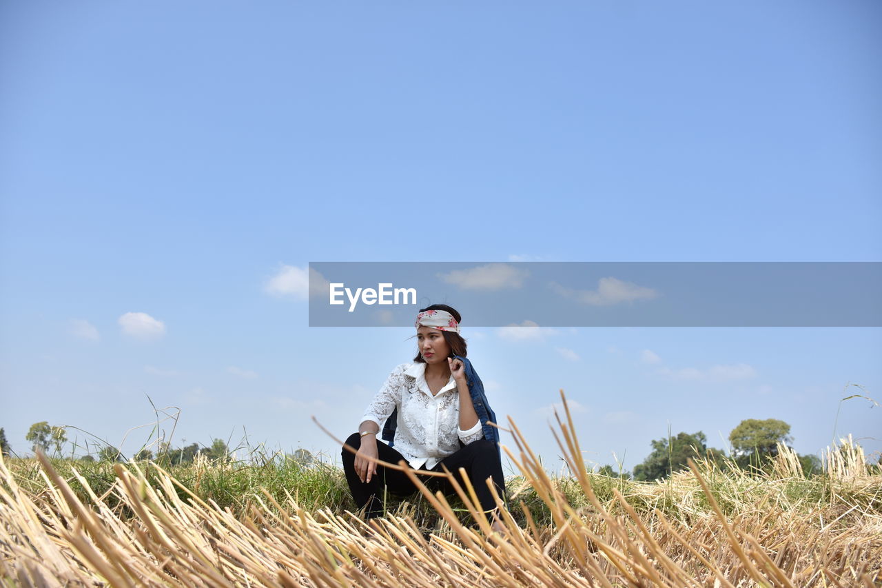 Woman crouching on field against blue sky