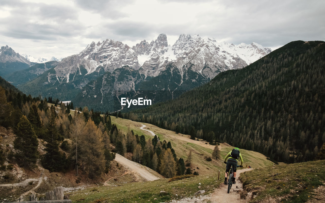 Rear view of man cycling on trail against sky