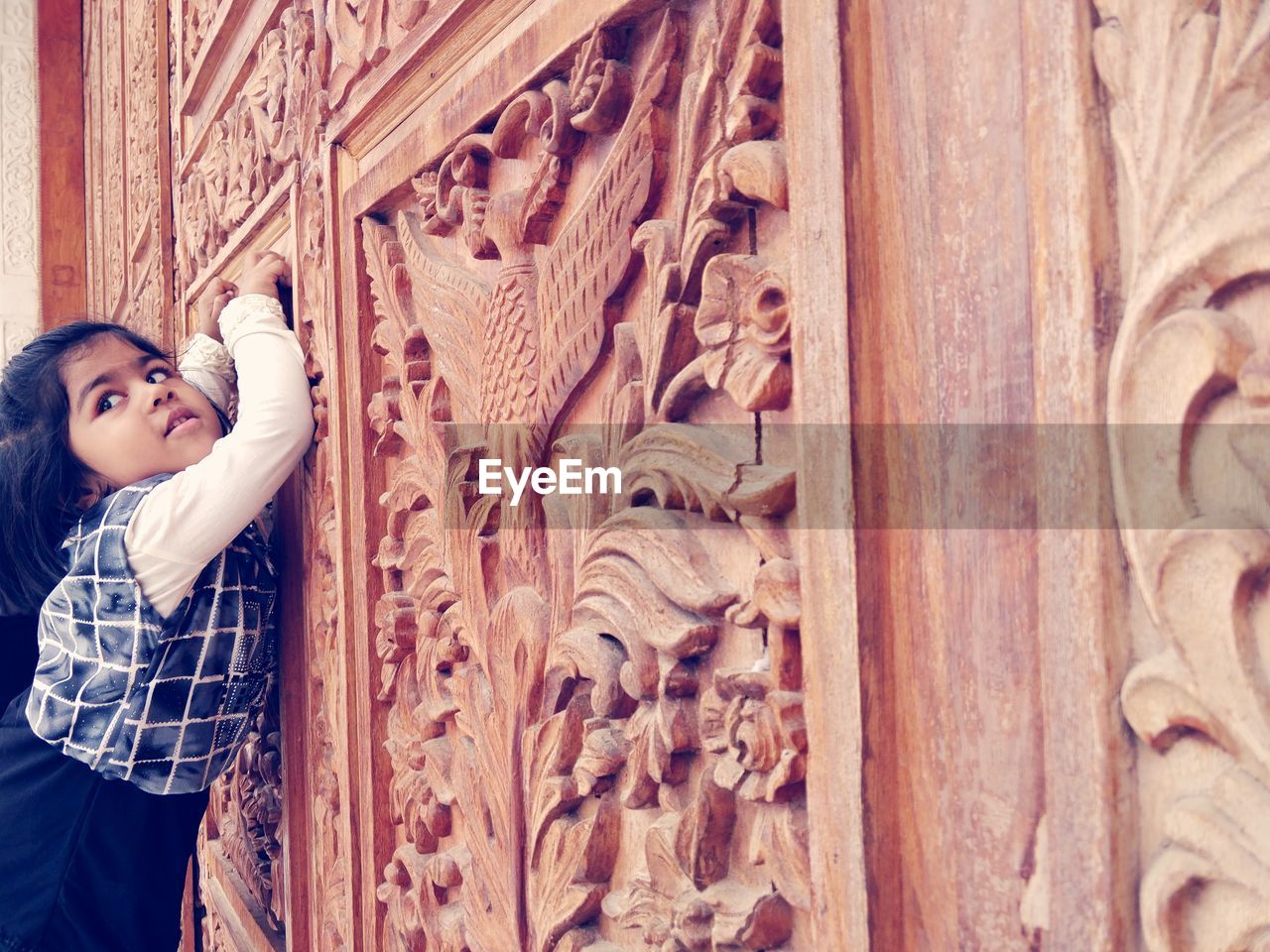 Side view of girl looking away while leaning on carved wall