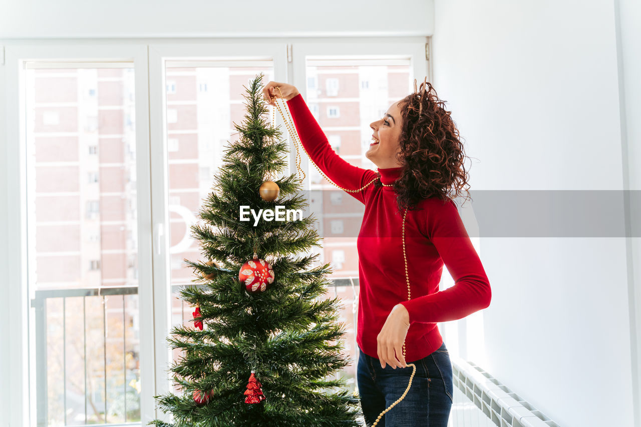 Side view of woman decorating christmas tree at home