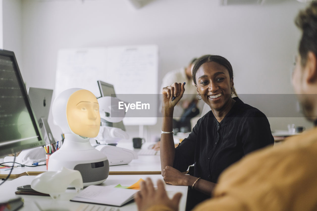 Smiling female phd student discussing with man at desk in innovation lab