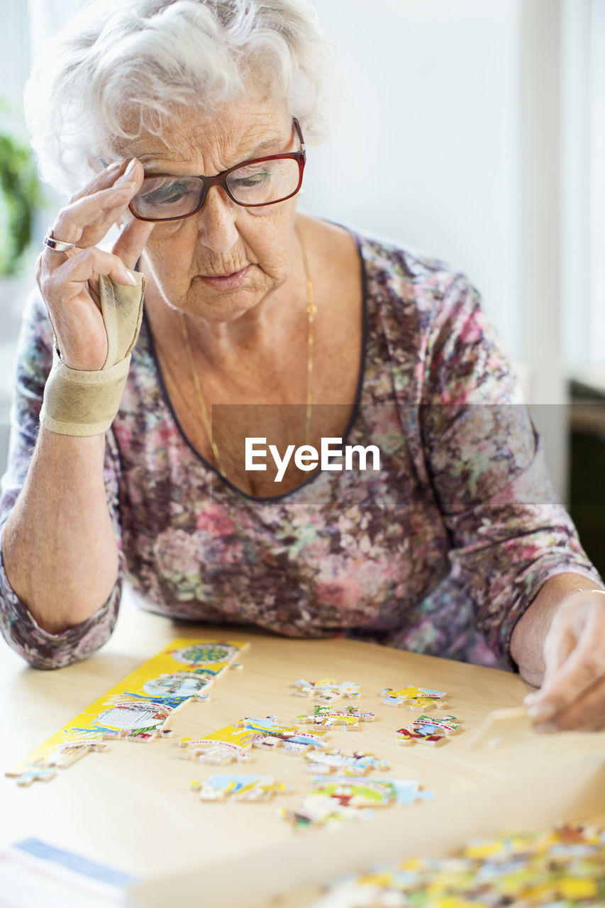 Senior woman solving jigsaw puzzle at table in nursing home