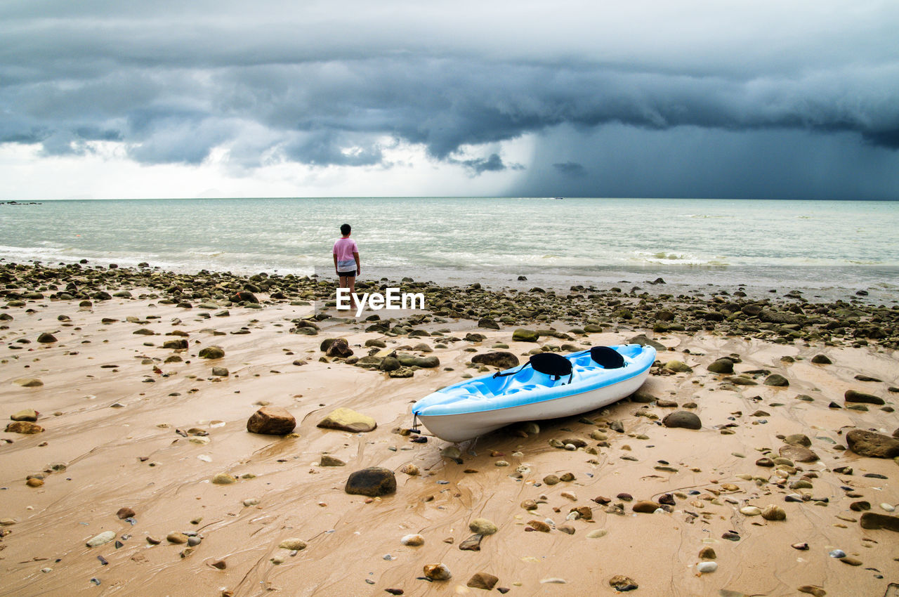 Rear view of boy standing on beach against sky