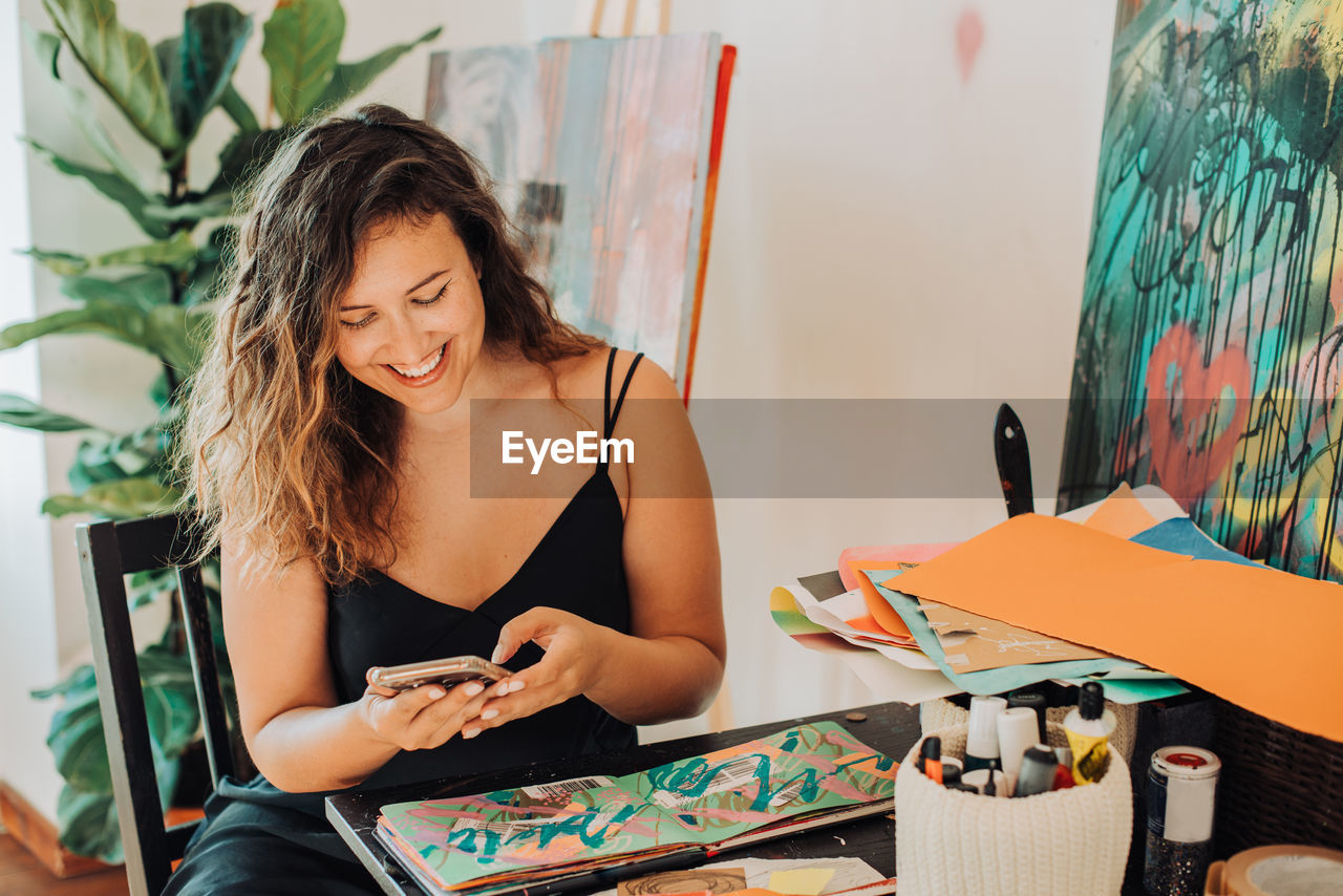 Female painter using smartphone while working on paintings in studio