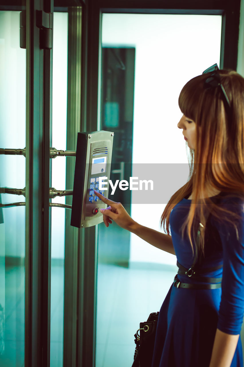 Side view of young woman using elevator buttons