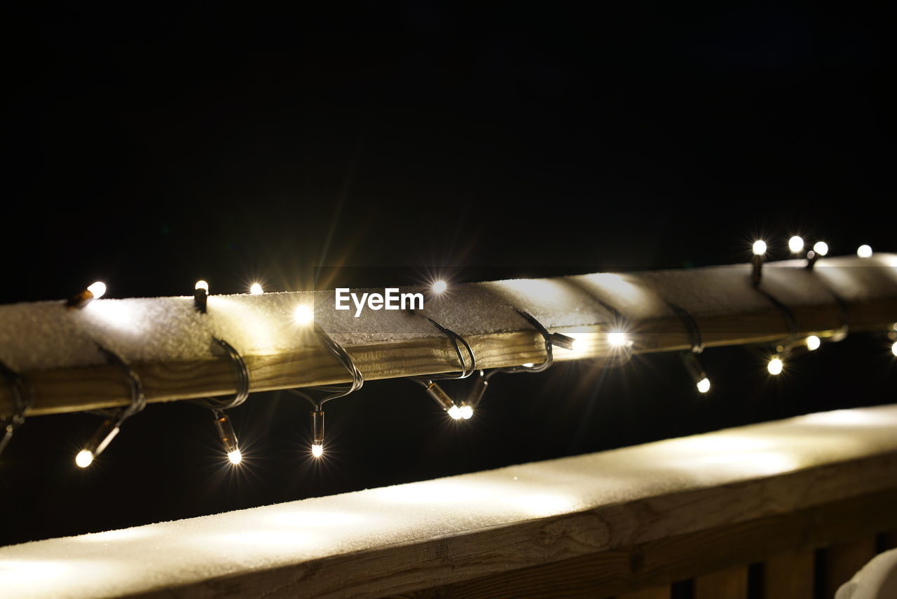 Illuminated christmas lights on railing with snow at night