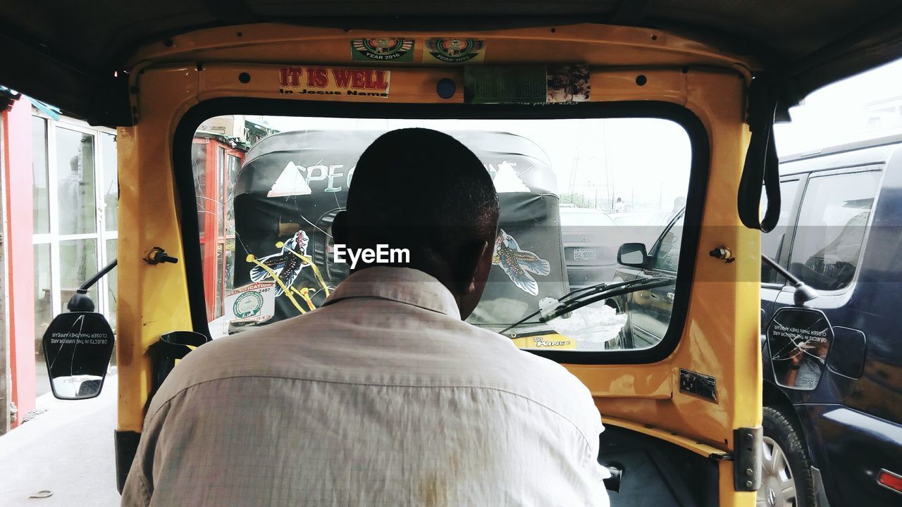 REAR VIEW OF MAN SITTING IN VEHICLE