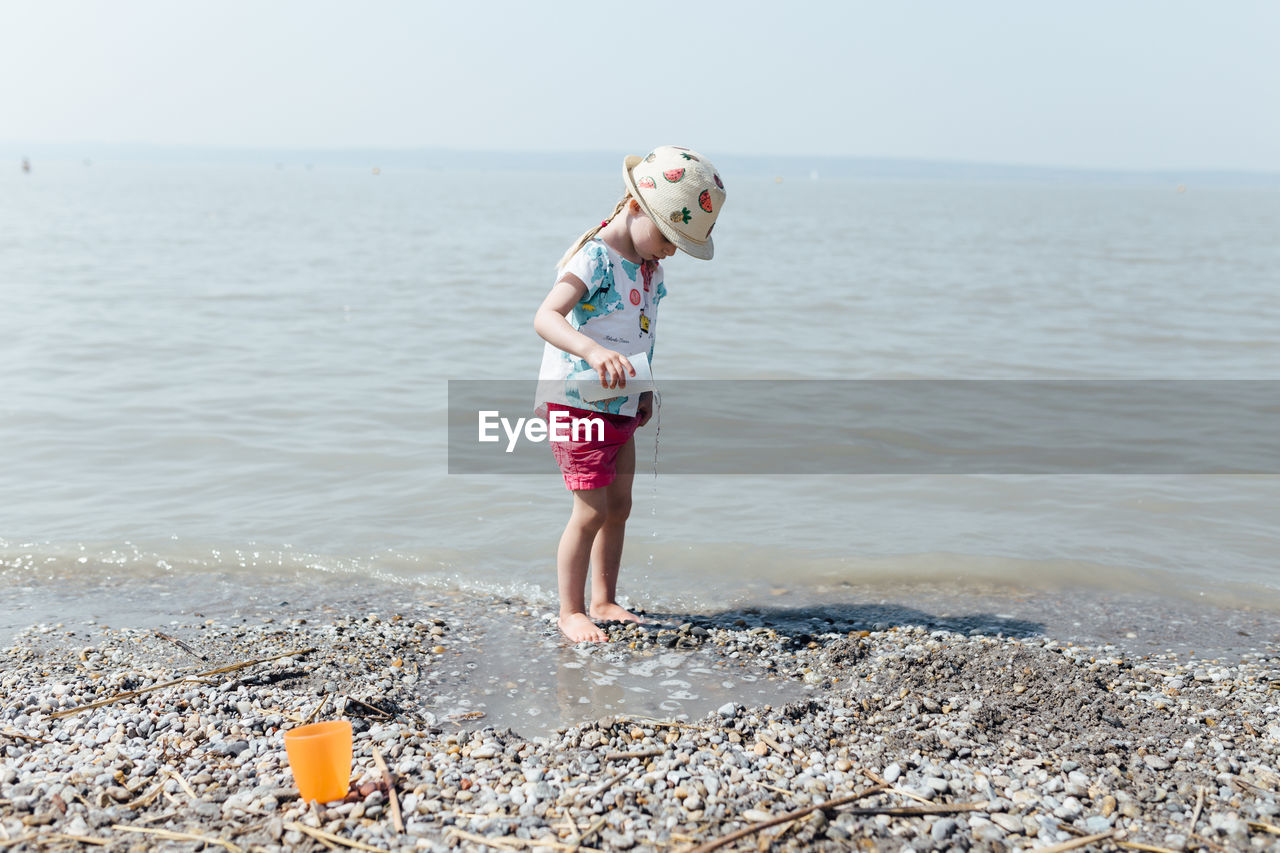 Full length of girl pouring water while standing on shore at beach