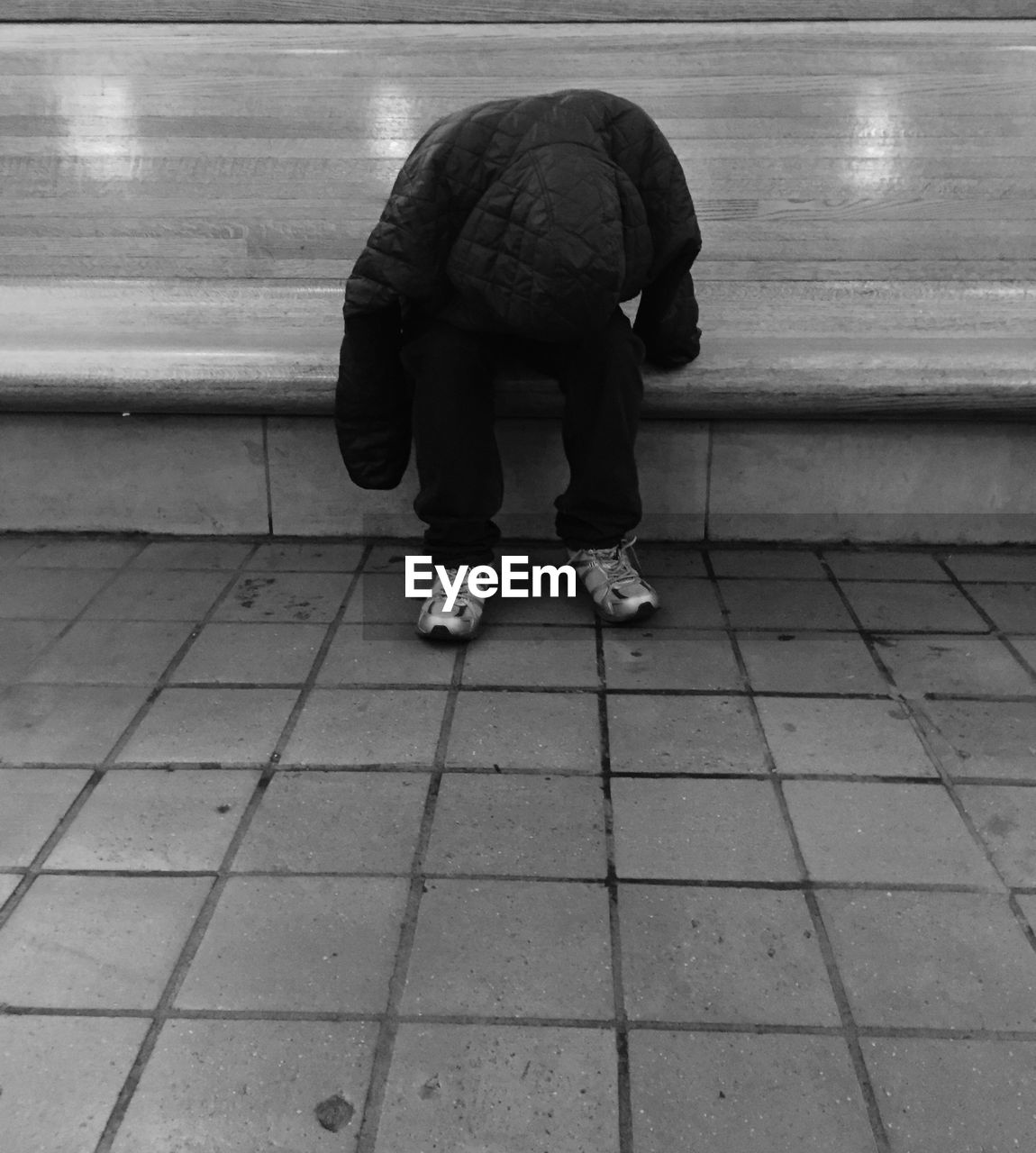 Homeless man wearing hood while sitting on retaining wall