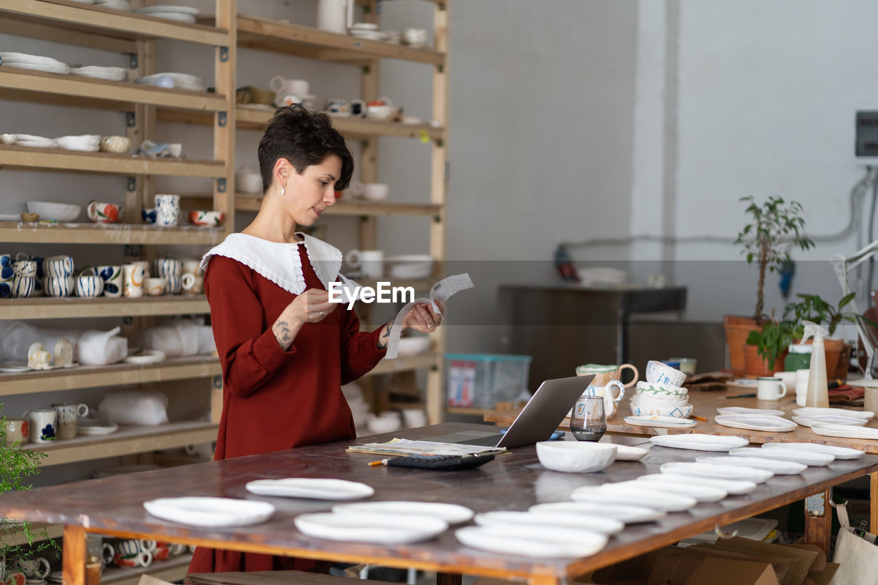 Female pottery studio owner looking at receipts calculating material costs to make ceramic product