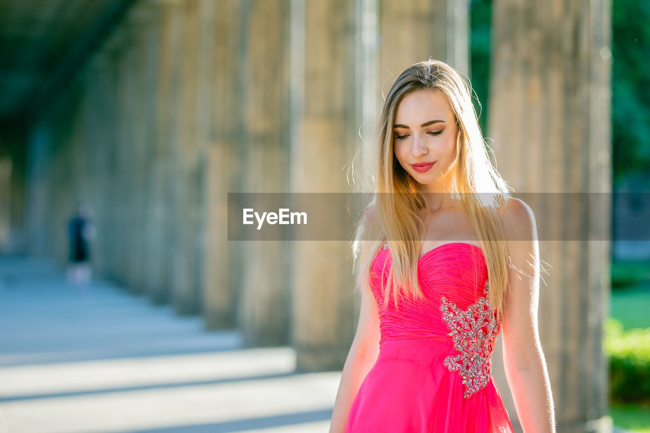 Beautiful young woman in pink evening dress standing at colonnade