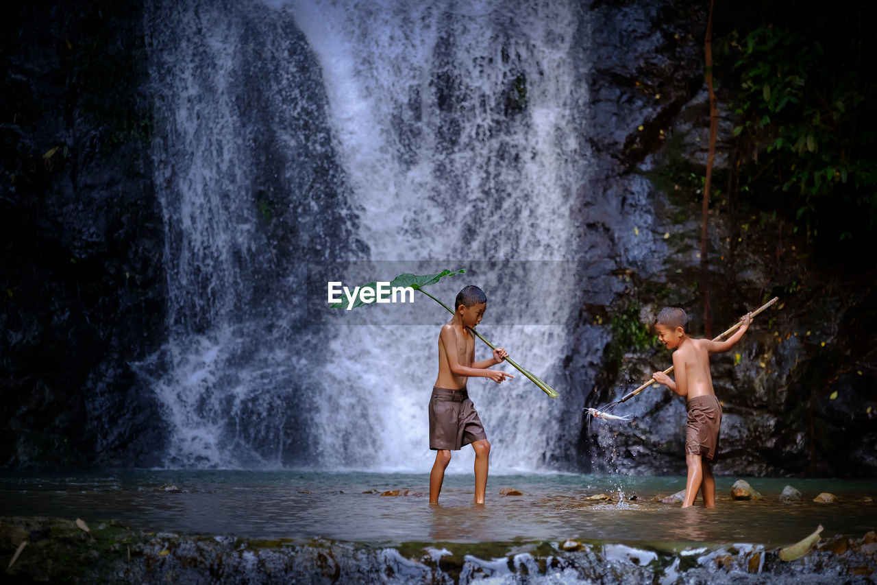 Full length of shirtless boys standing in river