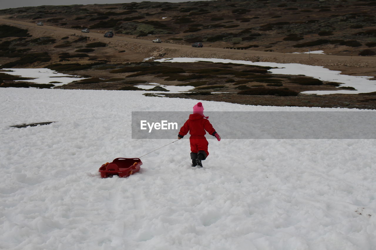 Rear view of child with sled walking on snow