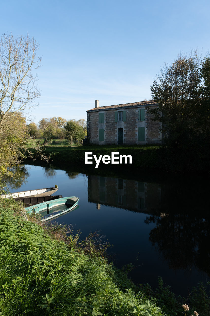 water, reflection, architecture, plant, tree, built structure, river, nature, sky, building exterior, waterway, building, house, no people, body of water, reservoir, moat, pond, blue, outdoors, residential district, day, tranquility, travel destinations, home, beauty in nature, clear sky, travel, mansion, history