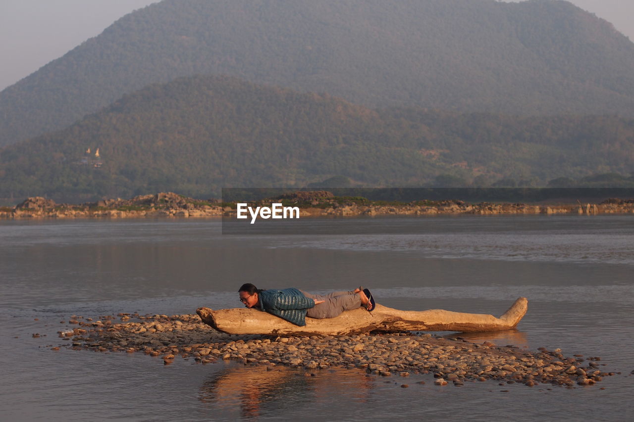Man lying on driftwood against mountain