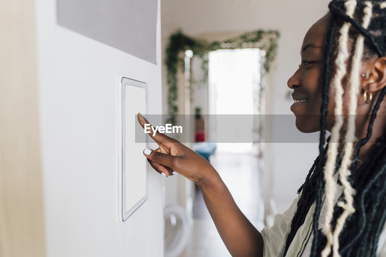 Smiling woman using home automation on wall at home