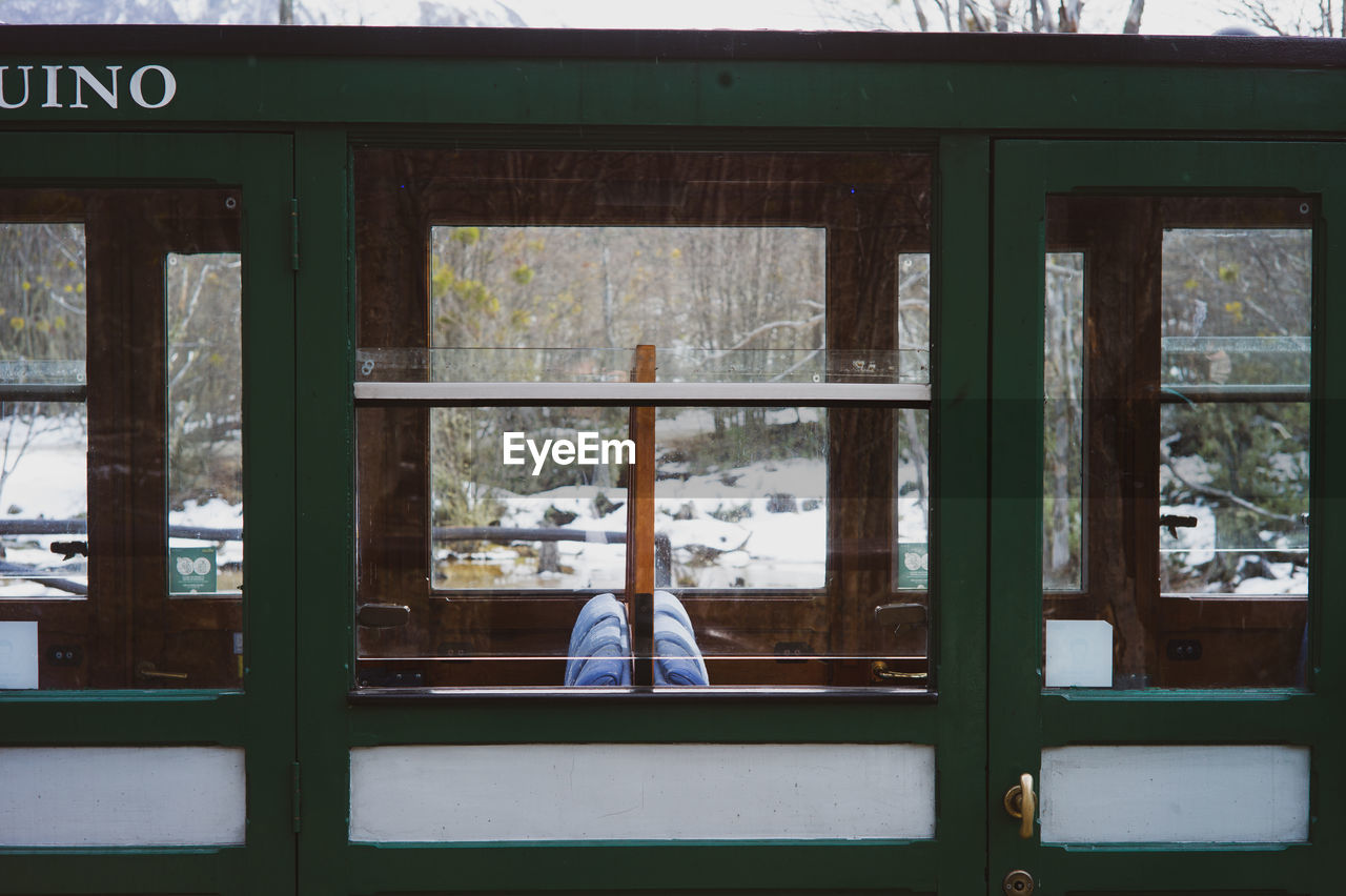REAR VIEW OF WOMAN SITTING ON WINDOW