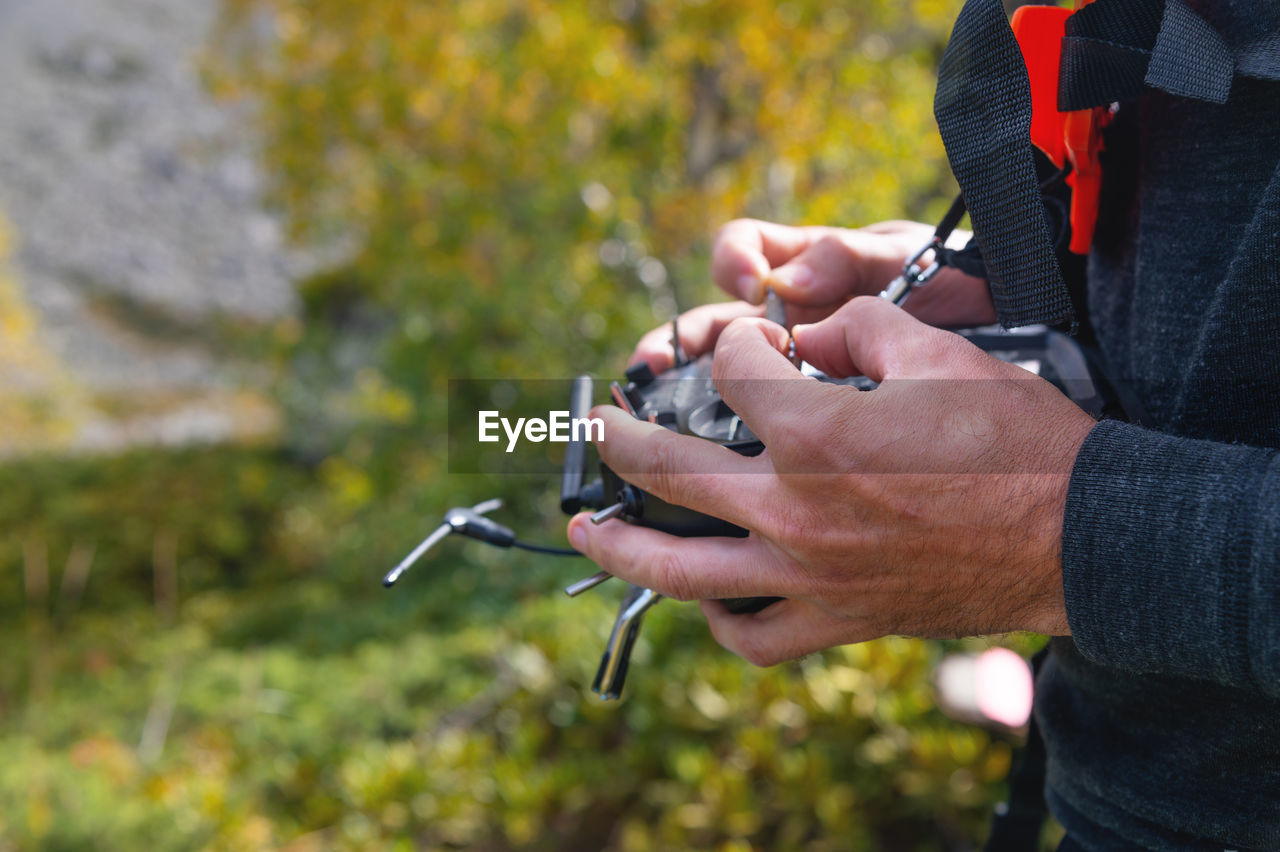 Male hands holding sticks on the remote control of a drone, close-up, outdoors