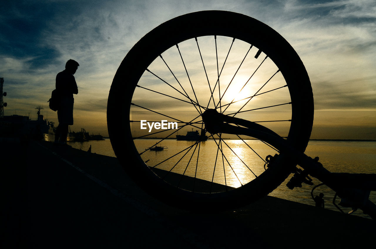 Silhouette people standing by bicycle against sky during sunset