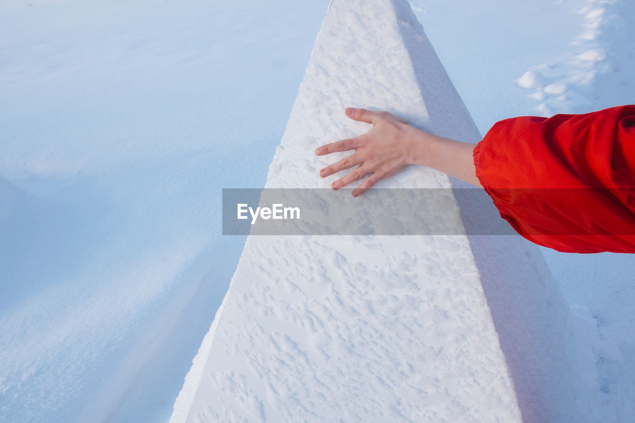 Cropped hand of woman touching snow covered retaining wall