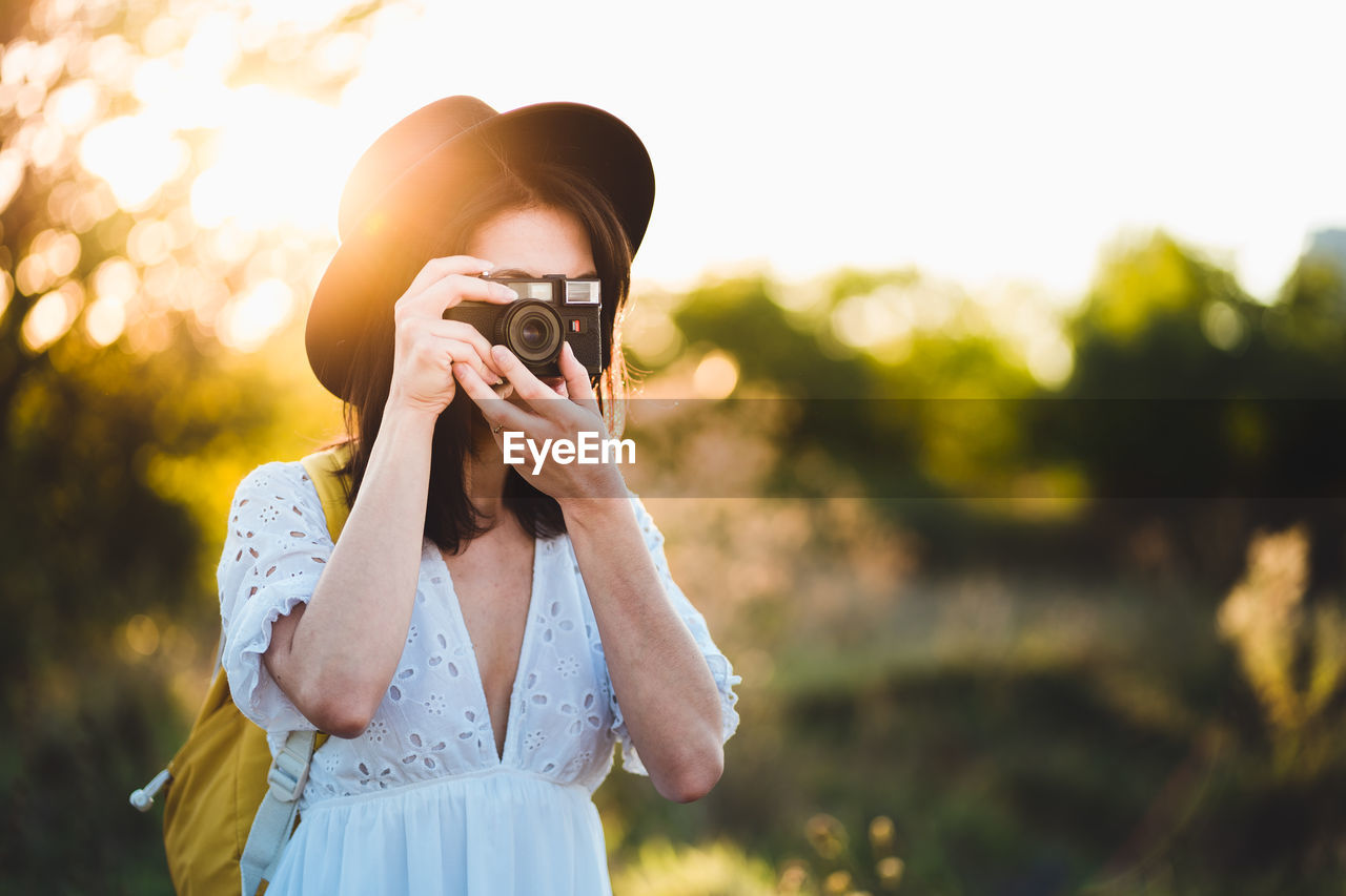 YOUNG WOMAN PHOTOGRAPHING AGAINST CAMERA